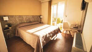 A hotel room with a bed, bedside table, lamp, chair, and a view of the outdoors. - Hôtel Le Panoramic (La Palud-sur-Verdon)