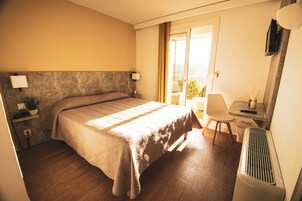 Quarto de hotel com cama, mesa de cabeceira, abajur, cadeira e vista para o exterior.