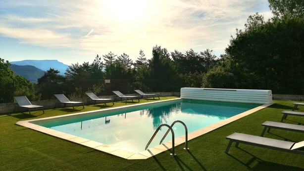 A swimming pool with a view of mountains, surrounded by grass and trees. - Hôtel Le Panoramic (La Palud-sur-Verdon)
