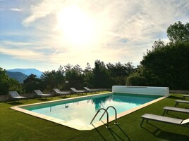 Piscina com vista para montanhas, cercada por grama e árvores.