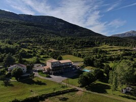 Um edifício grande com vários quartos, piscina e vista para a paisagem verde e montanhas ao redor.
