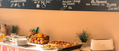 A buffet setup with a chalkboard menu, fruits, pastries, and a toaster.