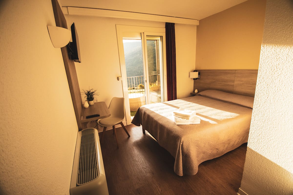 A hotel room with a bed, a chair, a desk, and a view of the outdoors.