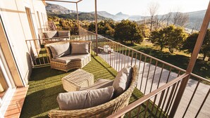 A balcony with wicker furniture, a view of mountains, and a grassy area. - Hôtel Le Panoramic (La Palud-sur-Verdon)