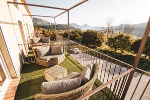 Uma varanda com móveis de vime, vista para montanhas e uma área gramada.