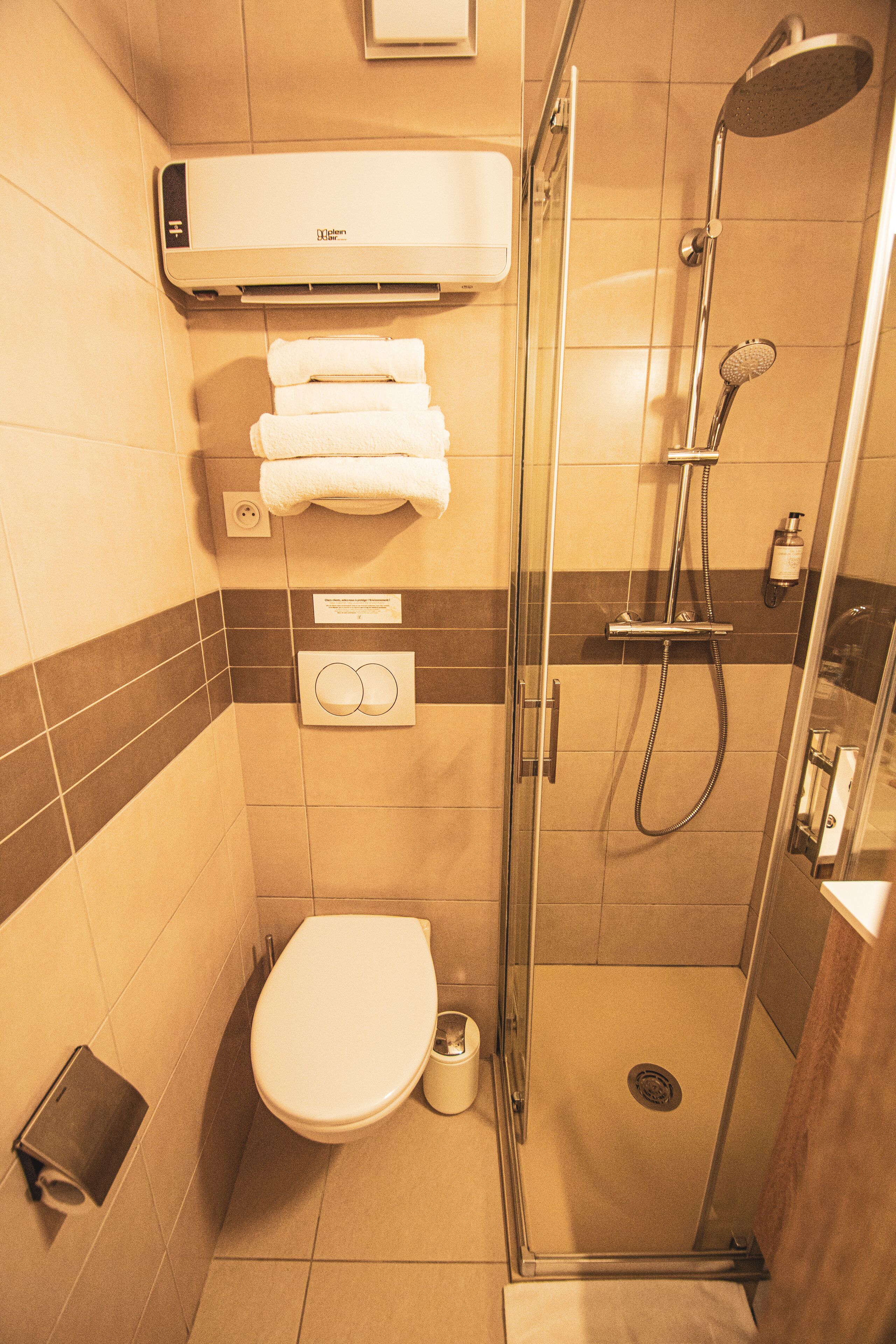 A compact bathroom with a toilet, a glass-enclosed shower, and a towel rack with folded towels.