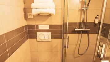 A compact bathroom with a toilet, a glass-enclosed shower, and a towel rack with folded towels.