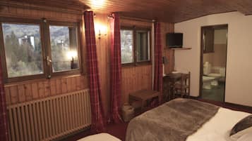 A wooden room with two beds, a television, a window with curtains, and a view of a forest.