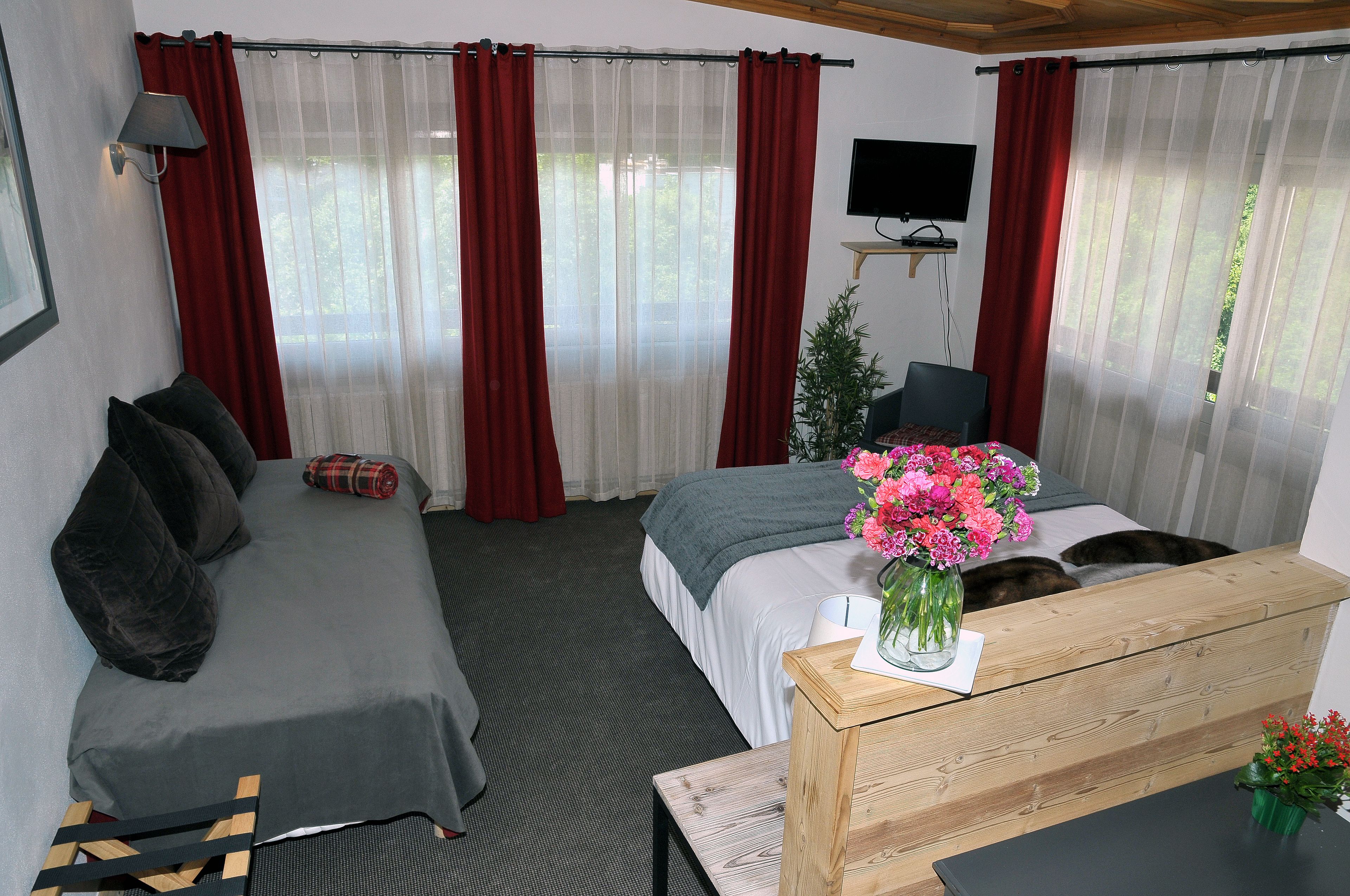A hotel room with a bed, a sofa, a TV, and a wooden table with a vase of flowers.