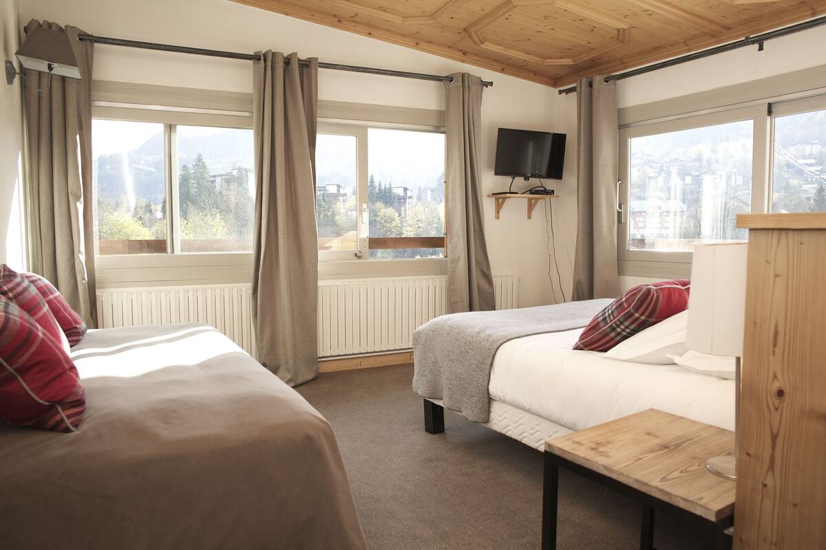 Una habitación con dos camas, televisión y vistas a un paisaje montañoso a través de amplios ventanales.