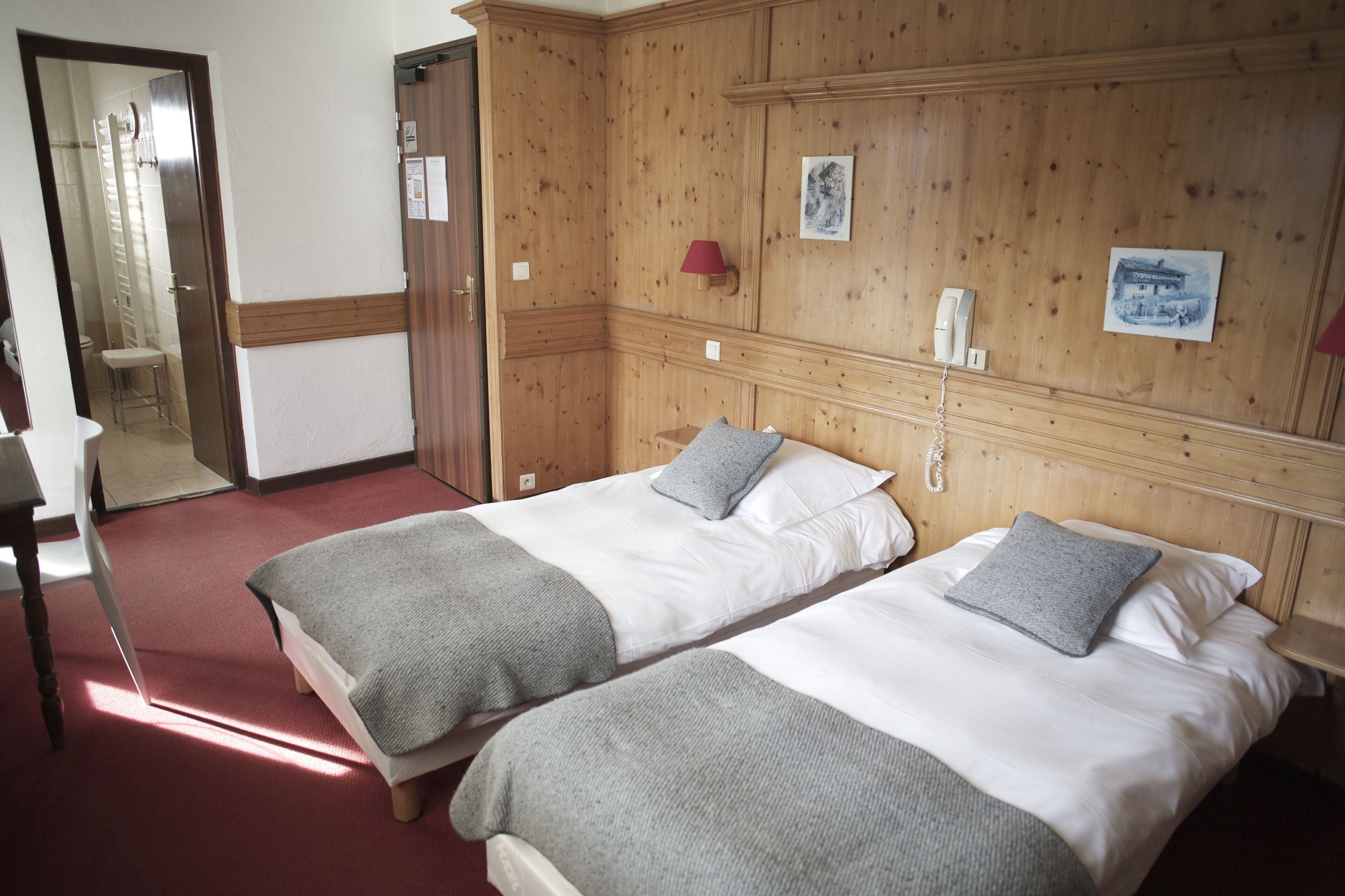 A hotel room with two beds, wooden paneling, a red carpet, and a small bathroom visible through an open door.