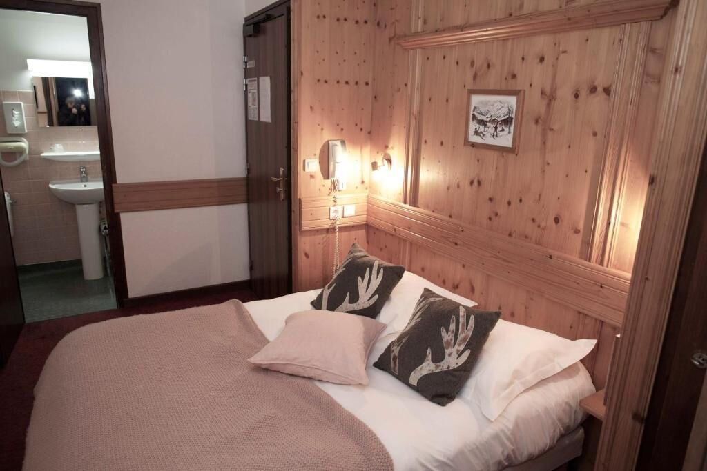 Un dormitorio con cabecera de madera, cama con ropa de cama blanca y marrón, y mesita de noche con una lámpara.