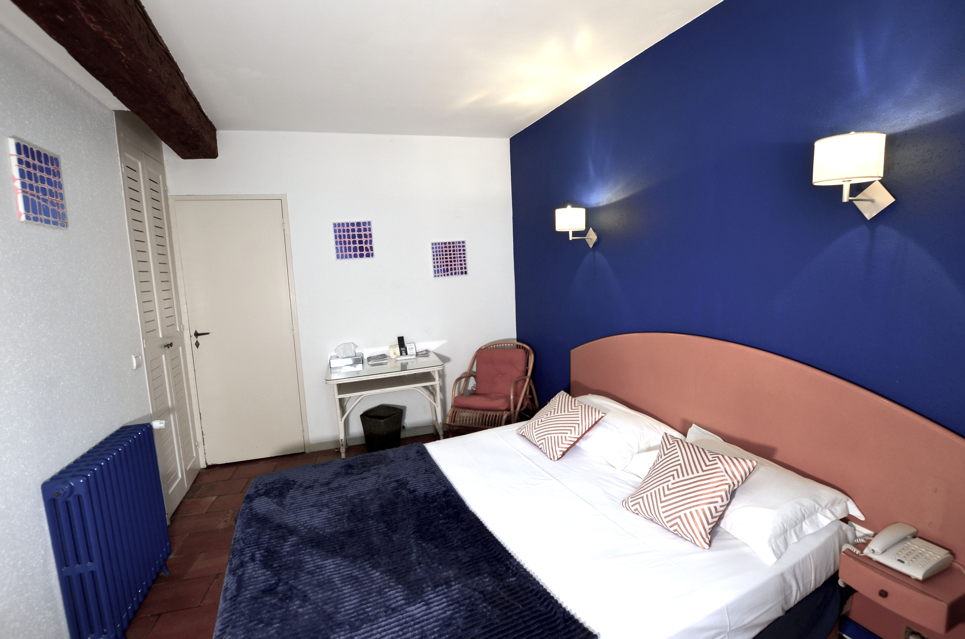 Una habitación de hotel con cama, escritorio, silla y radiador.