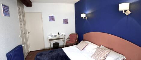 Una habitación de hotel con cama, escritorio, silla y radiador.