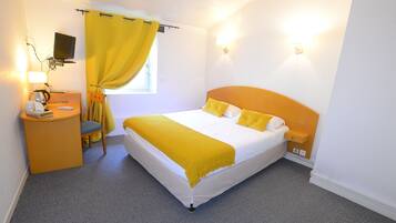 Une chambre d’hôtel équipée d’un lit, d’un bureau, d’une chaise, d’une télévision et d’une fenêtre avec des rideaux.