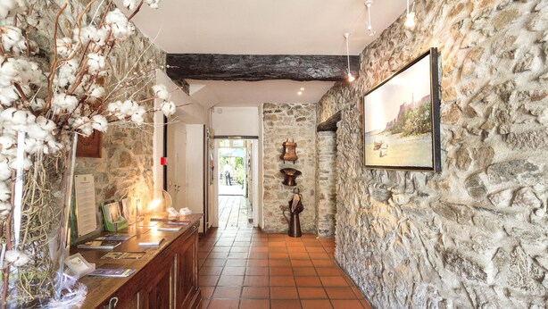A stone-walled hallway with a wooden reception desk, a hanging light fixture, and a framed picture on the wall.