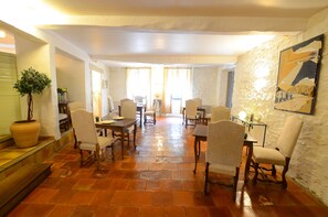 A dining area with a long table, multiple chairs, a potted plant, and a painting on the wall. - Hotel Restaurant du Midi (Revel)