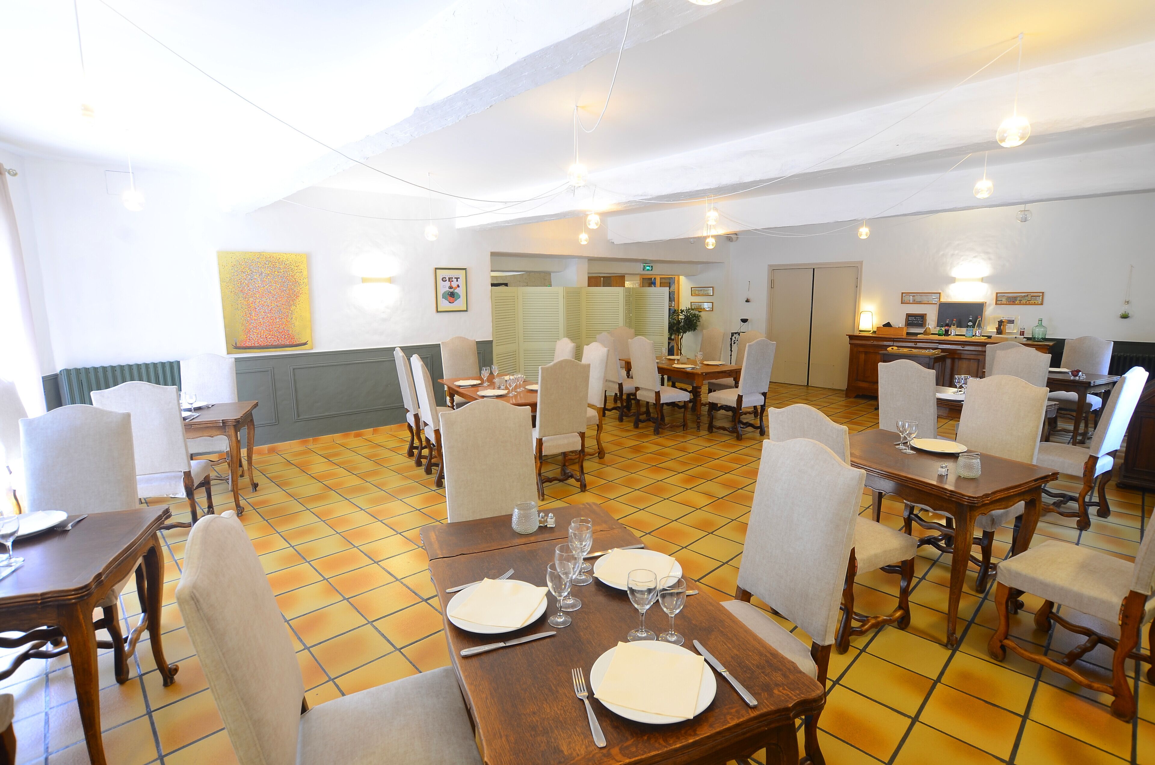 Un área de comedor con varias mesas y sillas, suelo de baldosas y una pared decorada con obras de arte.