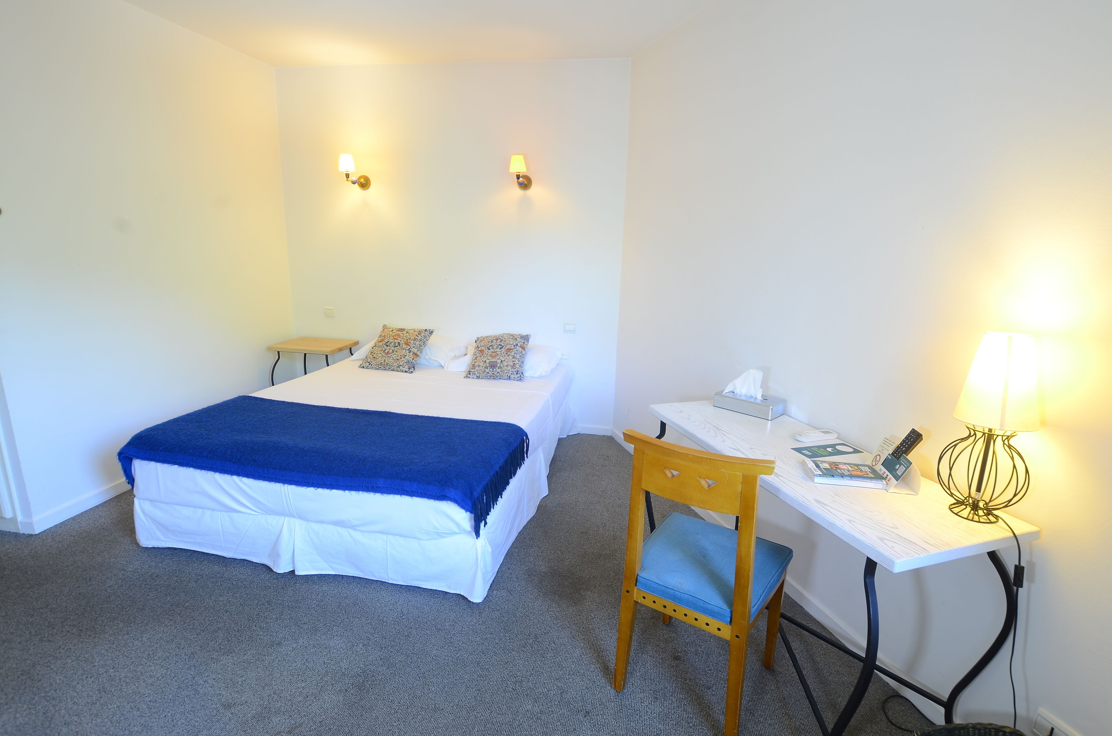 Una habitación de hotel con una cama, un escritorio, una silla y dos lámparas de pared.