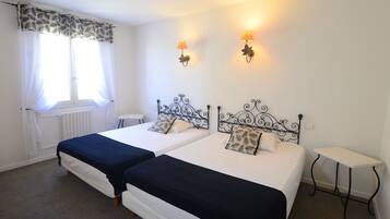Quarto de hotel com duas camas, uma janela com cortinas, um radiador e duas luminárias fixadas na parede.