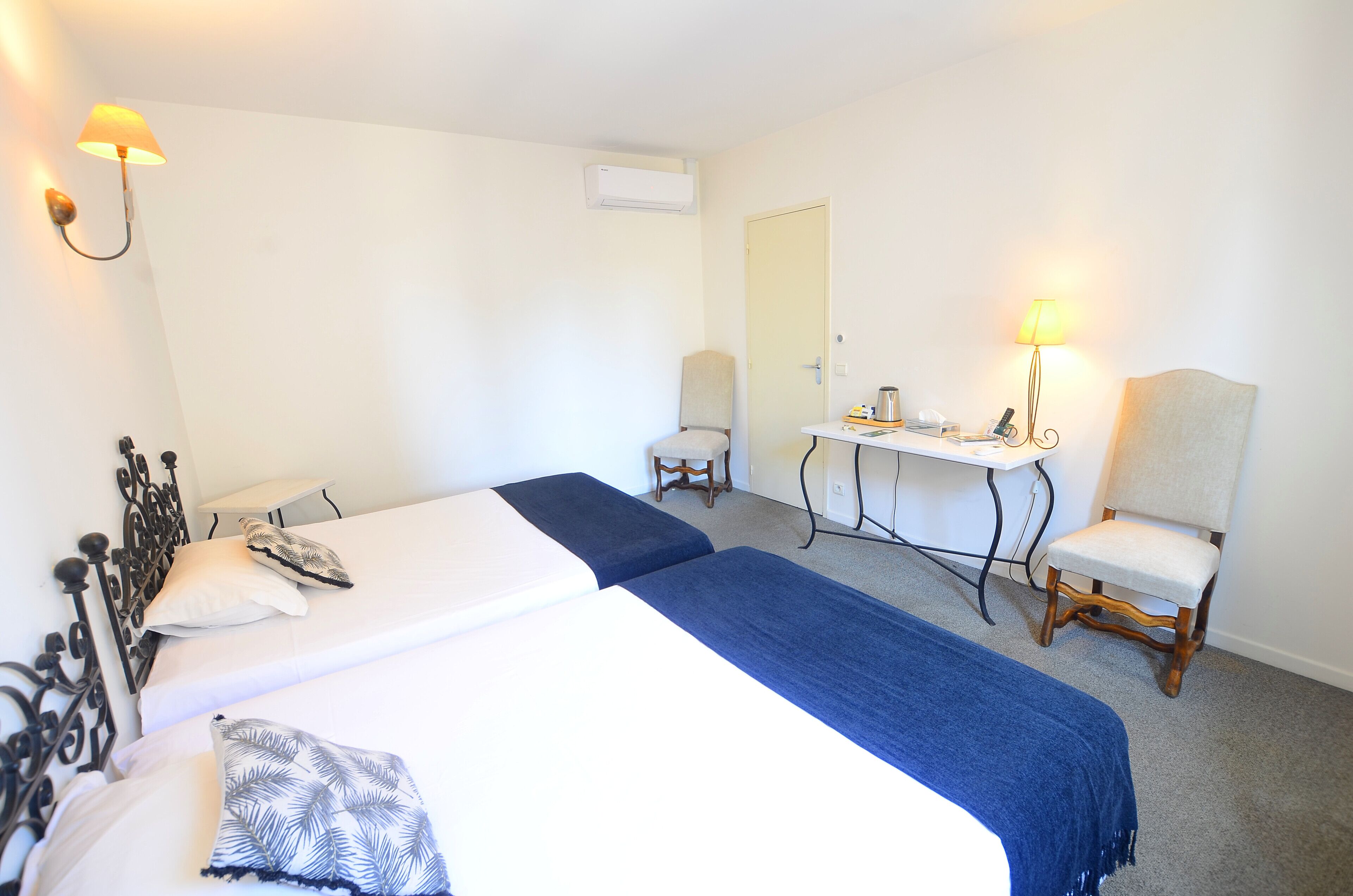 A hotel room with two beds, a desk, a chair, and a lamp.