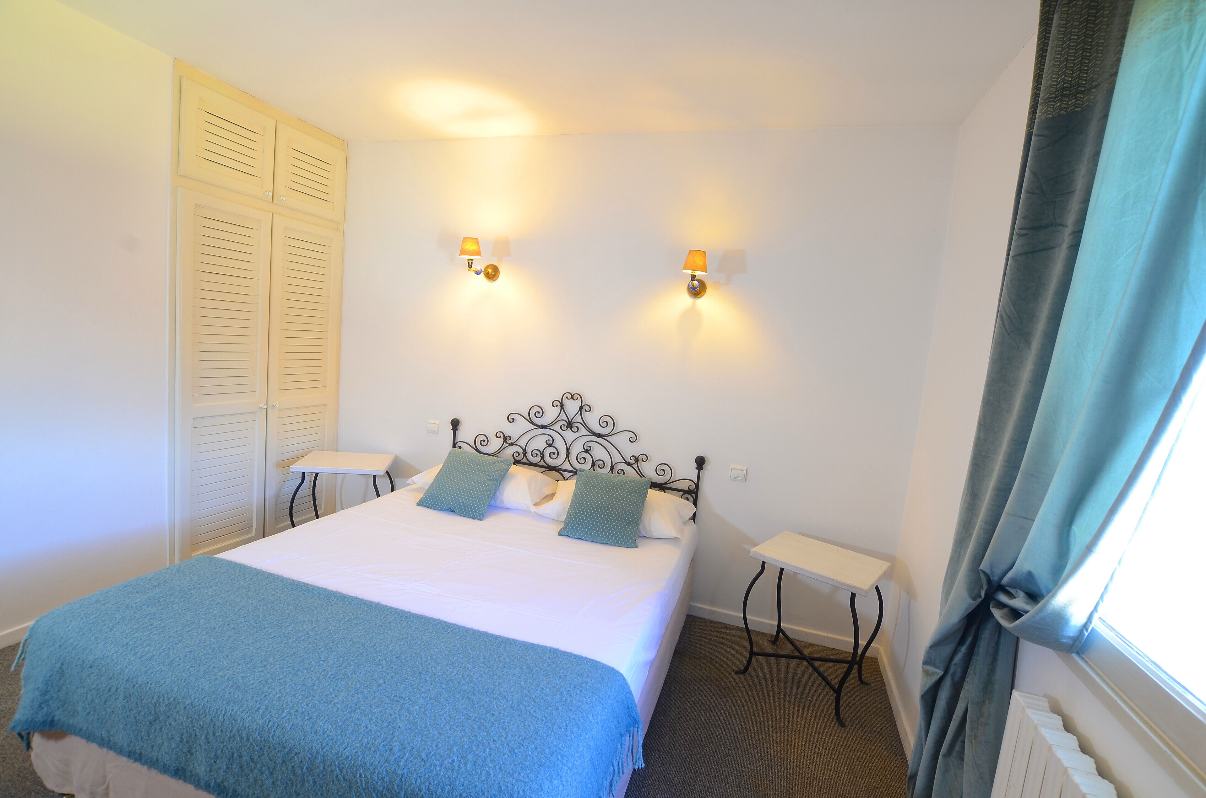 Une chambre à coucher comprenant un lit, deux tables de chevet, une armoire et deux lampes fixées au mur.