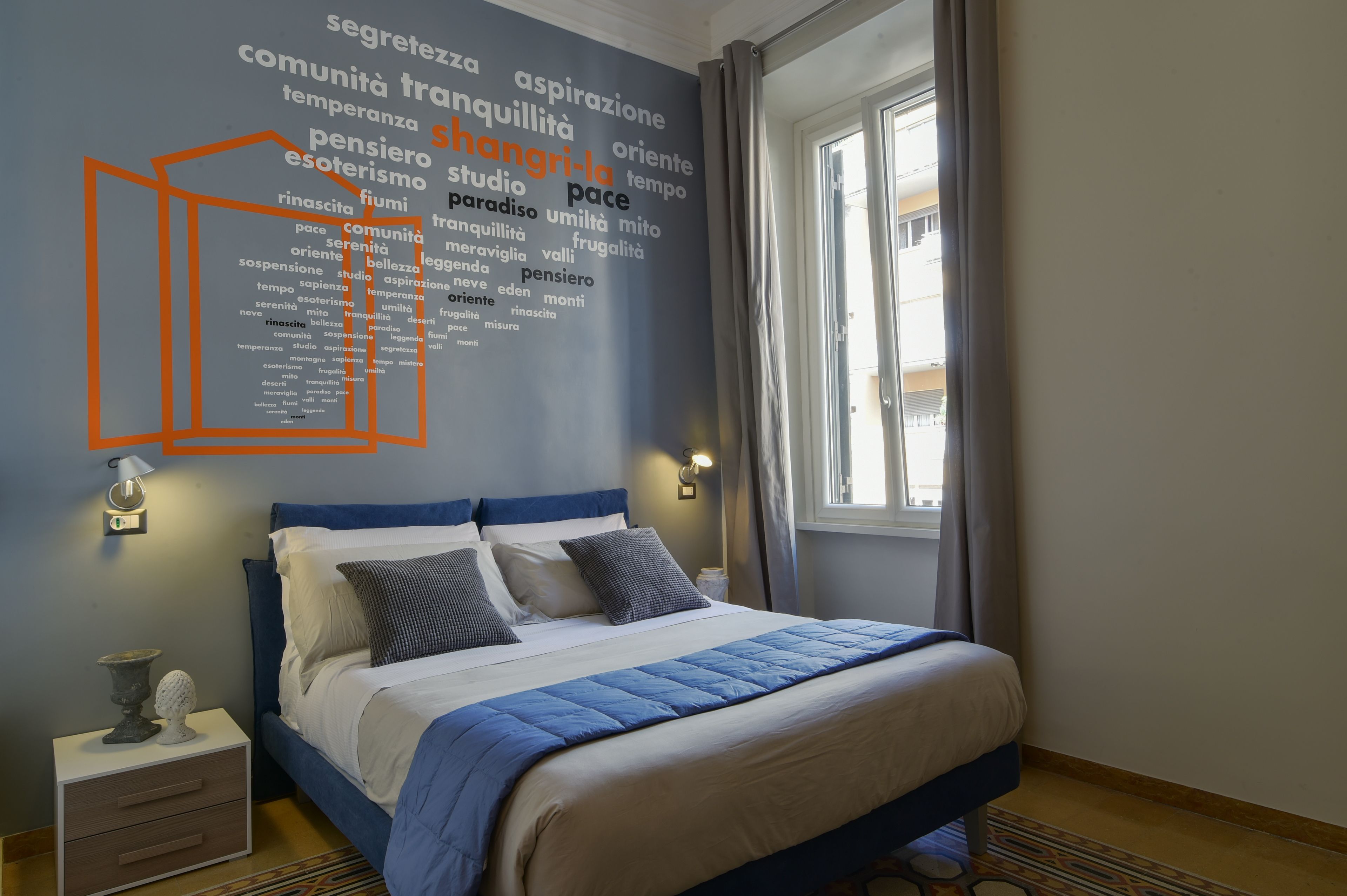 A bedroom with a bed, bedside tables, a wall with a word cloud, and a window.