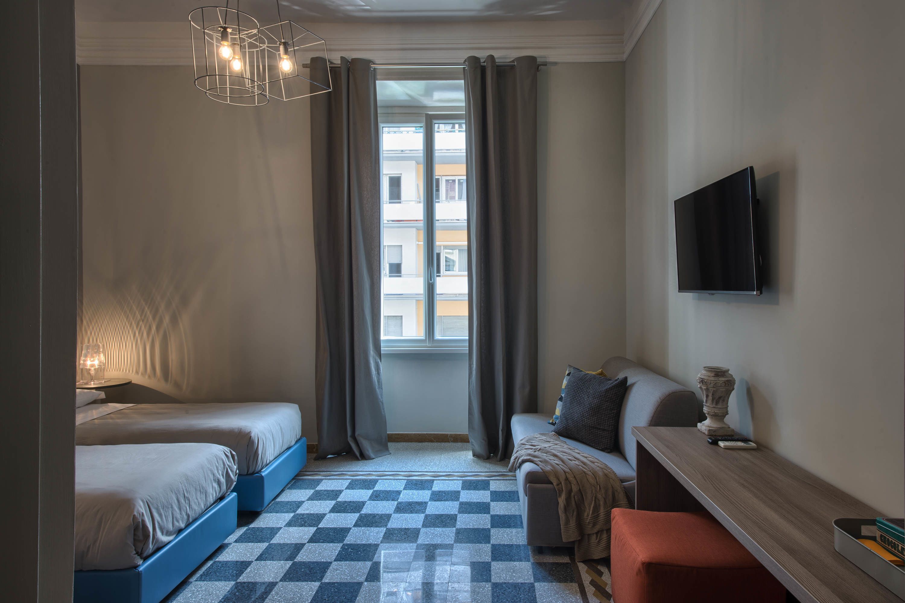 Ein Hotelzimmer mit zwei Betten, einem Schlafsofa, einem Fernseher und einem Fenster mit Vorhängen.