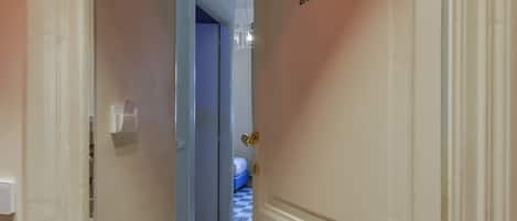 En gang med skakternet gulv, der fører til et værelse. En vandflaske ligger på gulvet.