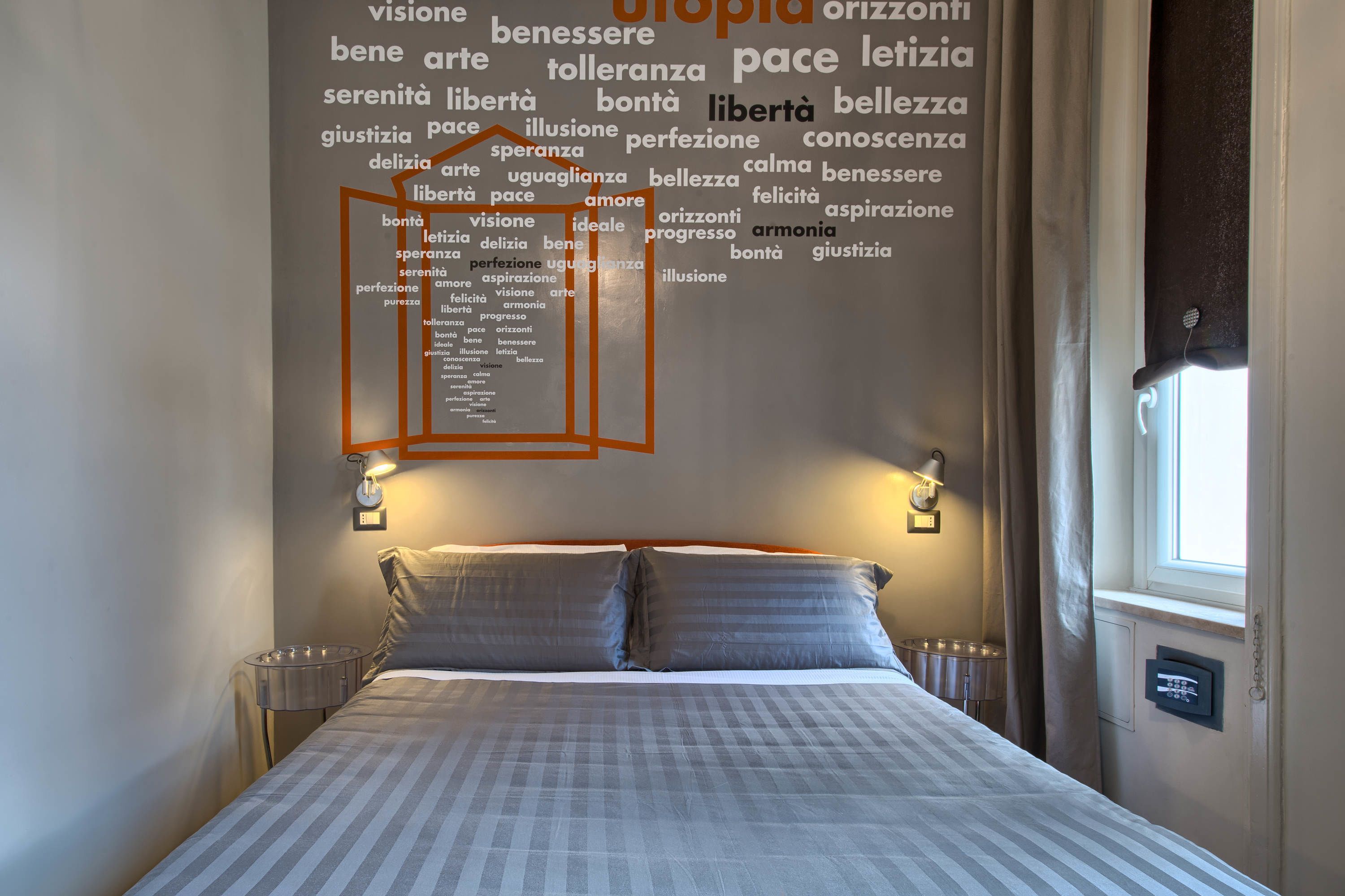 Habitación de hotel con una cama grande, dos mesitas de noche, una lámpara de pared y una ventana con cortinas.