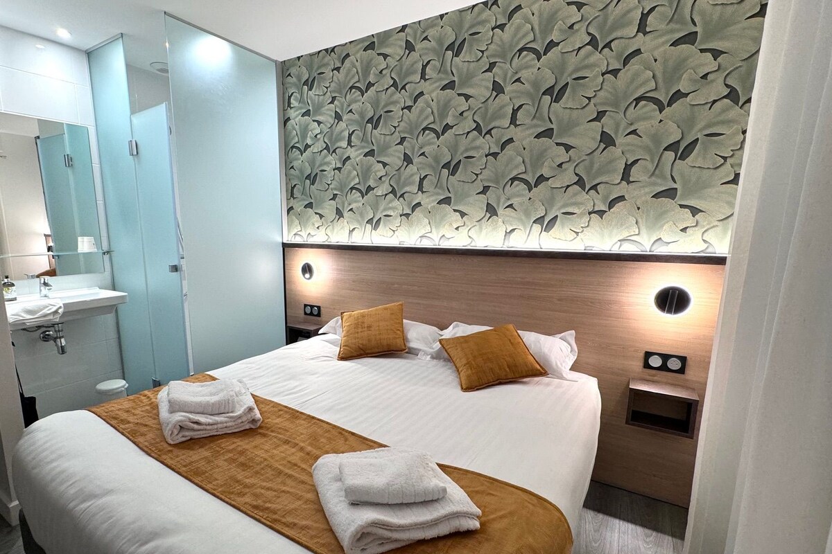Une chambre d’hôtel avec un lit, une salle de bain et un mur orné d’un motif de feuilles.