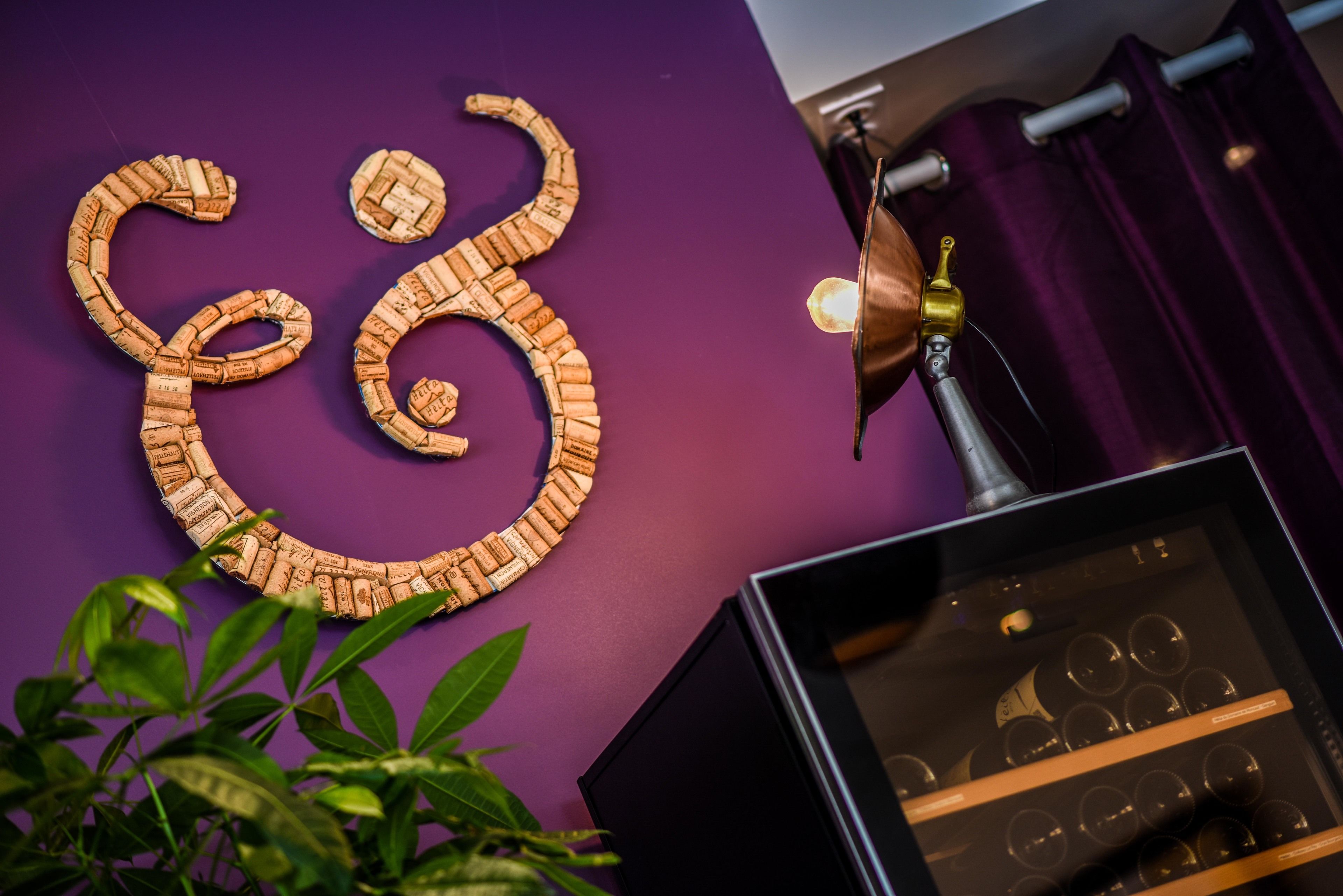 A cork art piece on a purple wall, a brass lamp, and a wine rack with bottles.