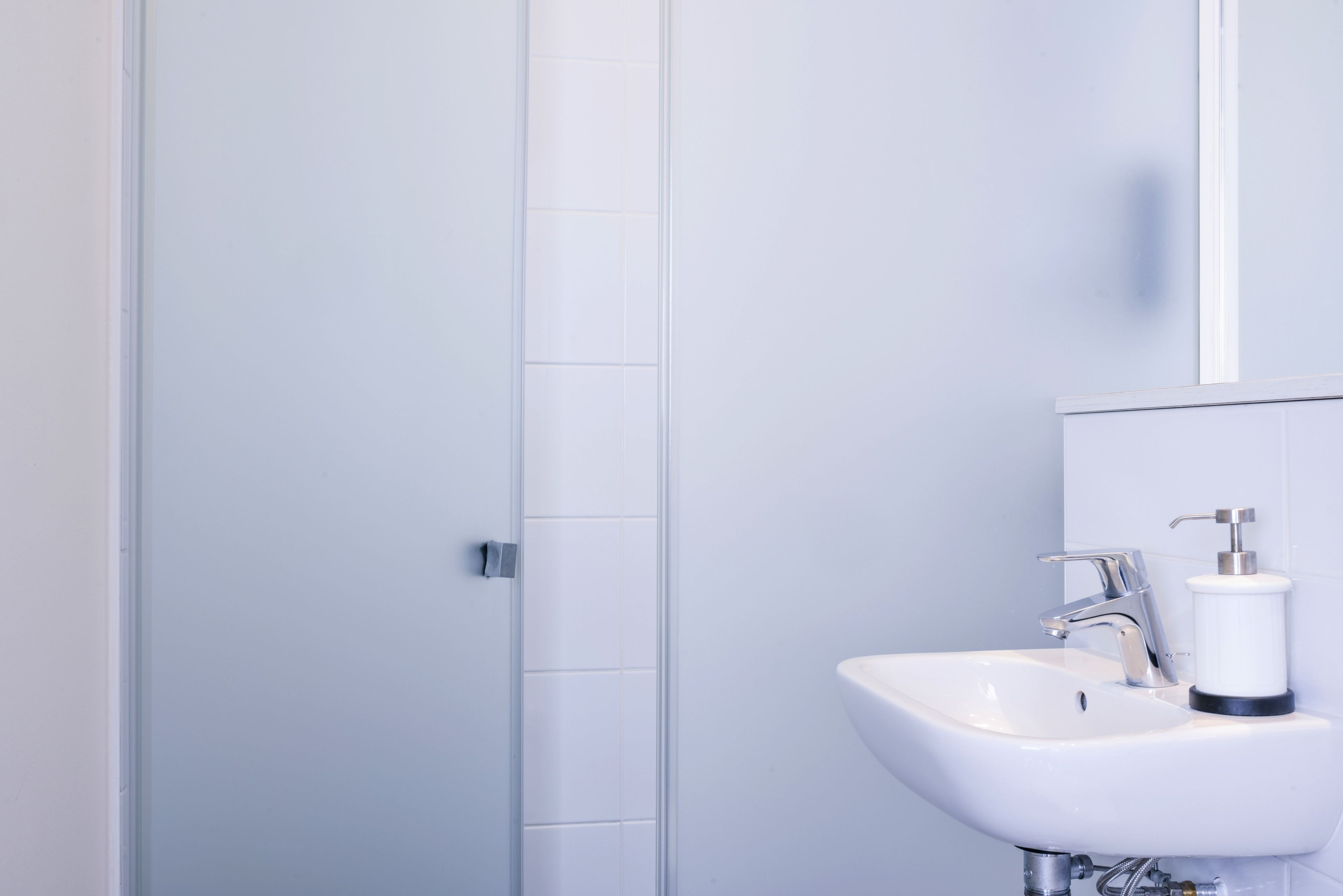 A modern bathroom with a white sink, chrome faucet, and a soap dispenser.