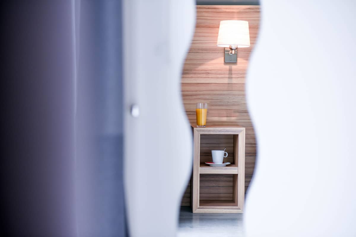 Une pièce avec un mur en bois, une petite étagère en bois sur laquelle se trouvent une tasse et un verre de jus d’orange, et une lampe fixée au mur.