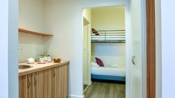 Une cuisine compacte avec un plan de travail en bois, un évier et un petit coin pour prendre le petit-déjeuner. On aperçoit un lit superposé avec des oreillers dans la pièce adjacente.
