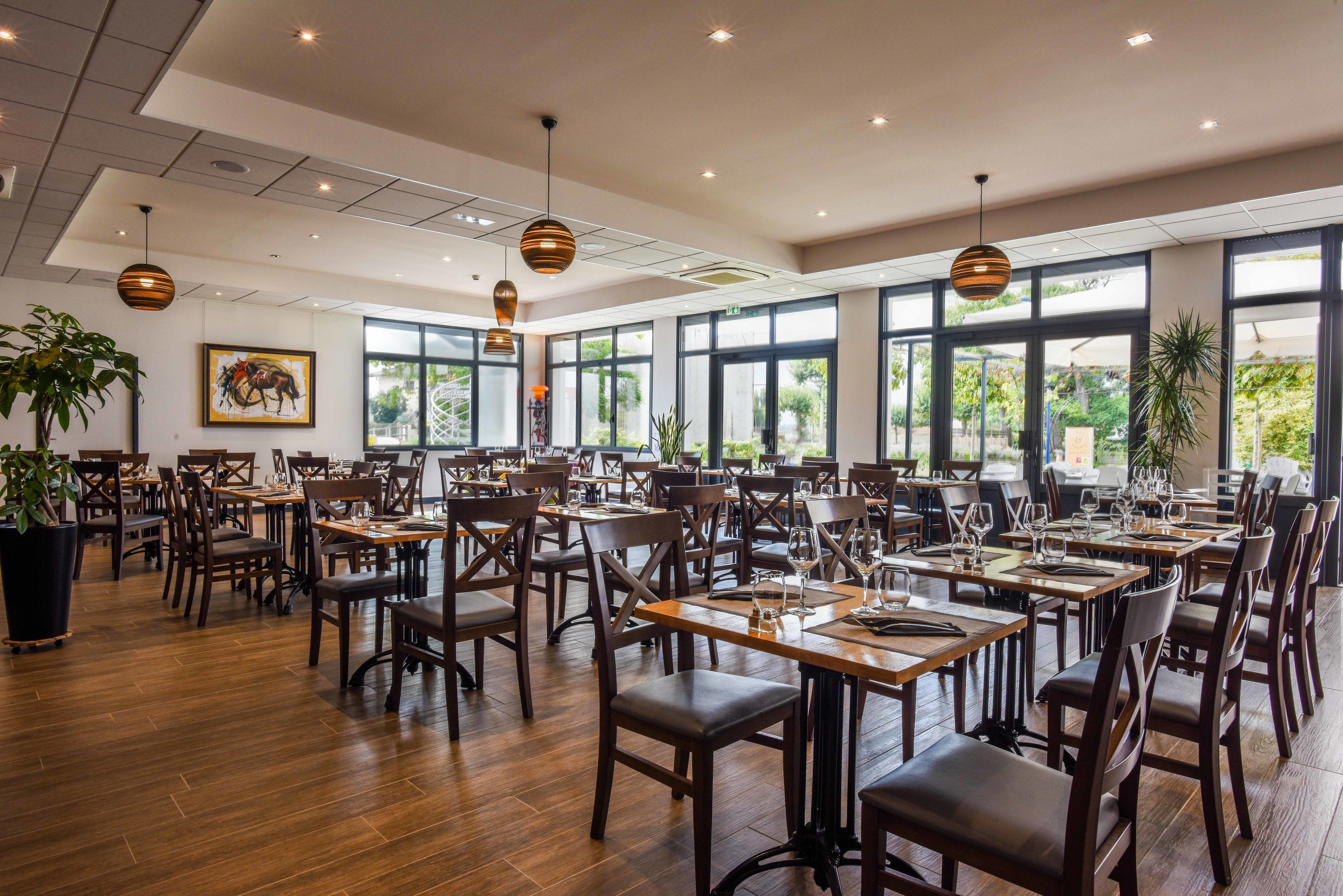 Un restaurante espacioso con mesas y sillas de madera, ventanas amplias y lámparas colgantes.