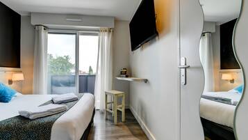 Habitación de hotel con dos camas, un televisor, una mesita y una ventana con cortinas.
