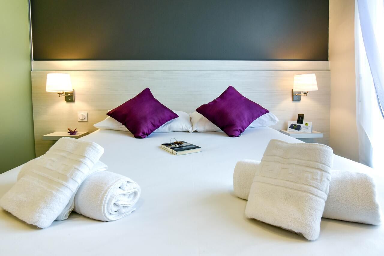 Une chambre d’hôtel avec un lit, deux oreillers, deux lampes de chevet, une table de chevet et deux serviettes enroulées.