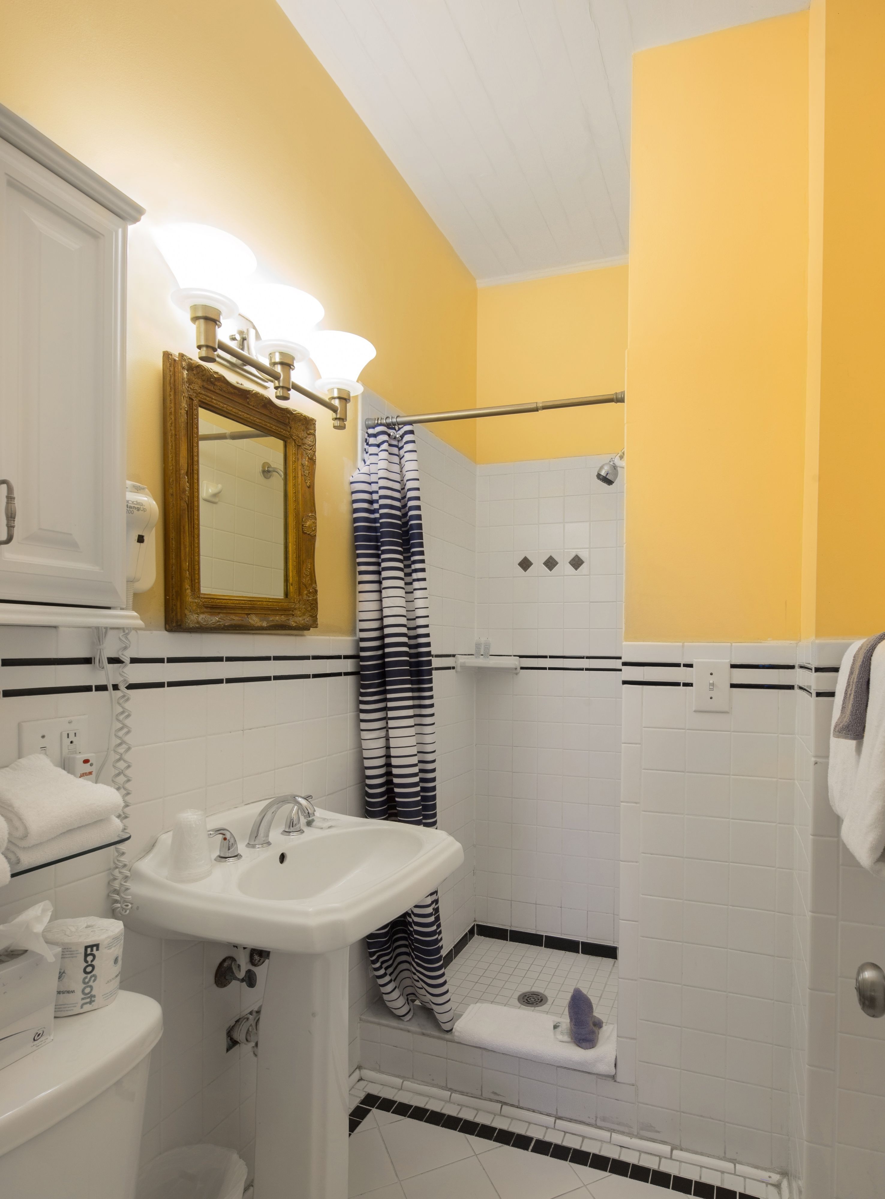 A bathroom with a white sink, a mirror with a gold frame, and a shower area with a striped curtain.