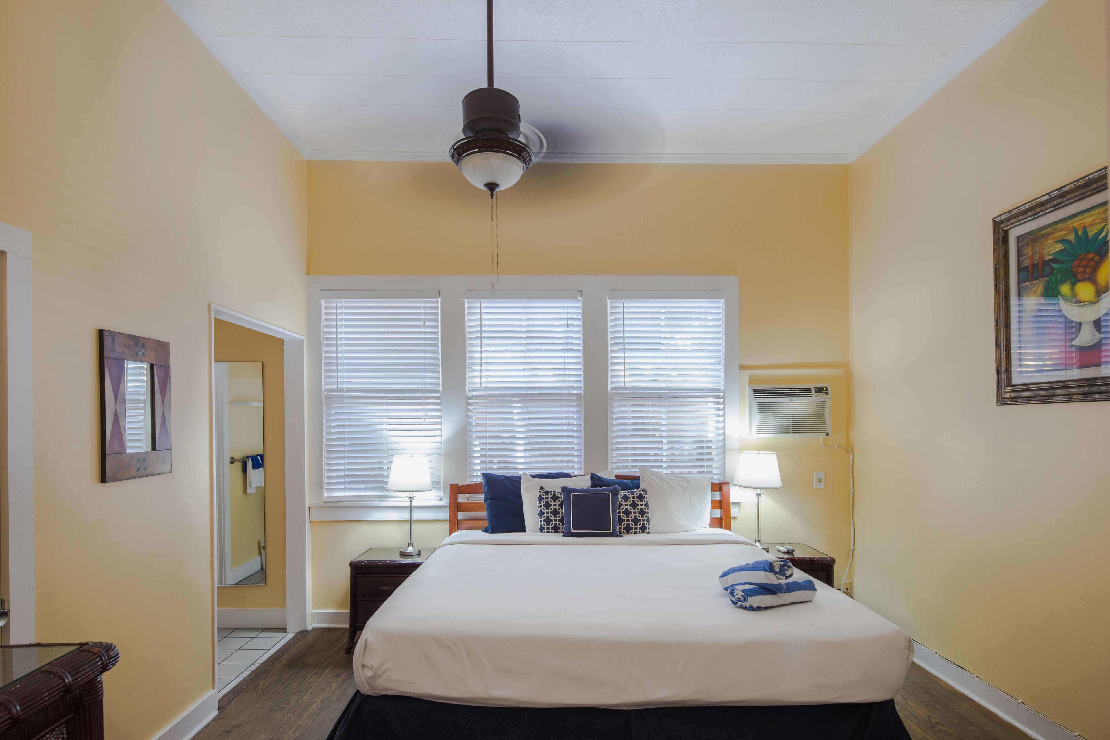 A hotel room with a bed, bedside tables, a ceiling fan, and a window with blinds.