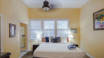 A hotel room with a bed, bedside tables, a ceiling fan, and a window with blinds.