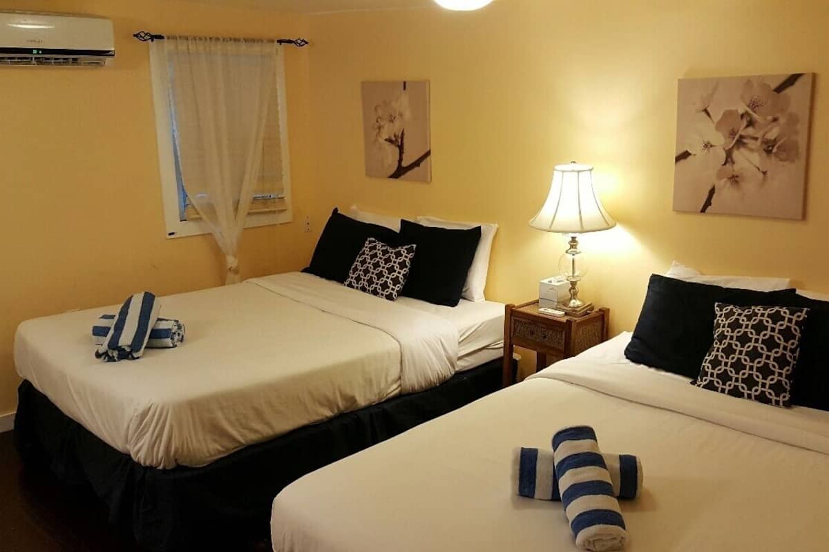 Two single beds with white linens, black and patterned pillows, a bedside table with a lamp, and wall art.