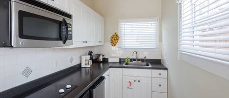 Una cocina moderna con armarios blancos, un microondas de acero inoxidable, una cafetera y un lavamanos.