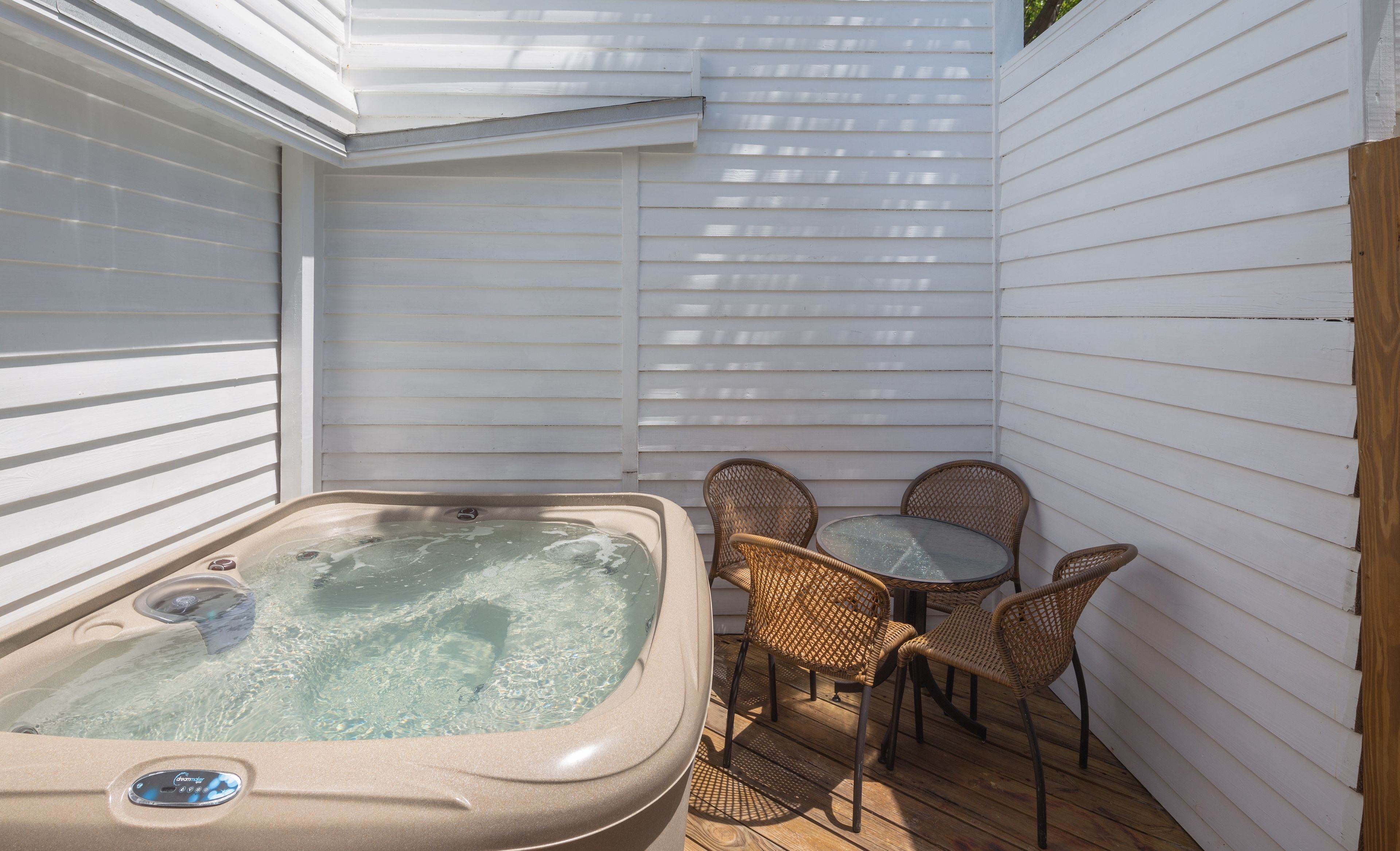 A hot tub with a control panel, surrounded by wicker chairs and a small table on a wooden deck.