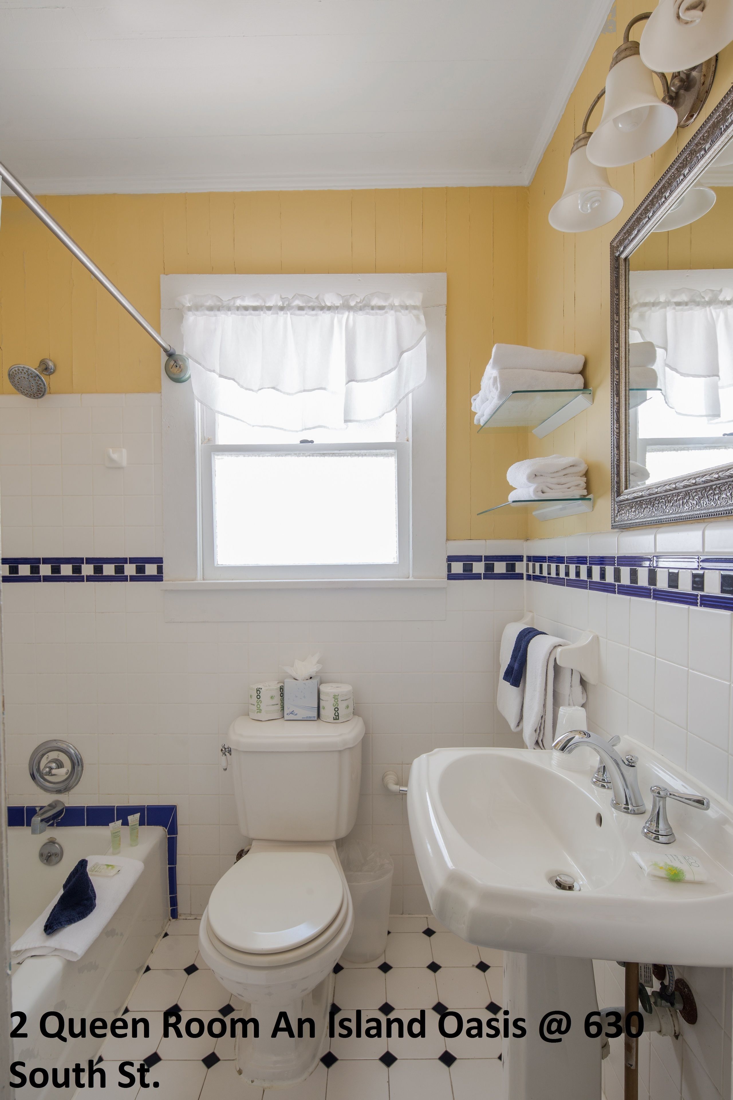A 2 Queen Room with a white toilet, a sink, a bathtub, and a window with curtains.