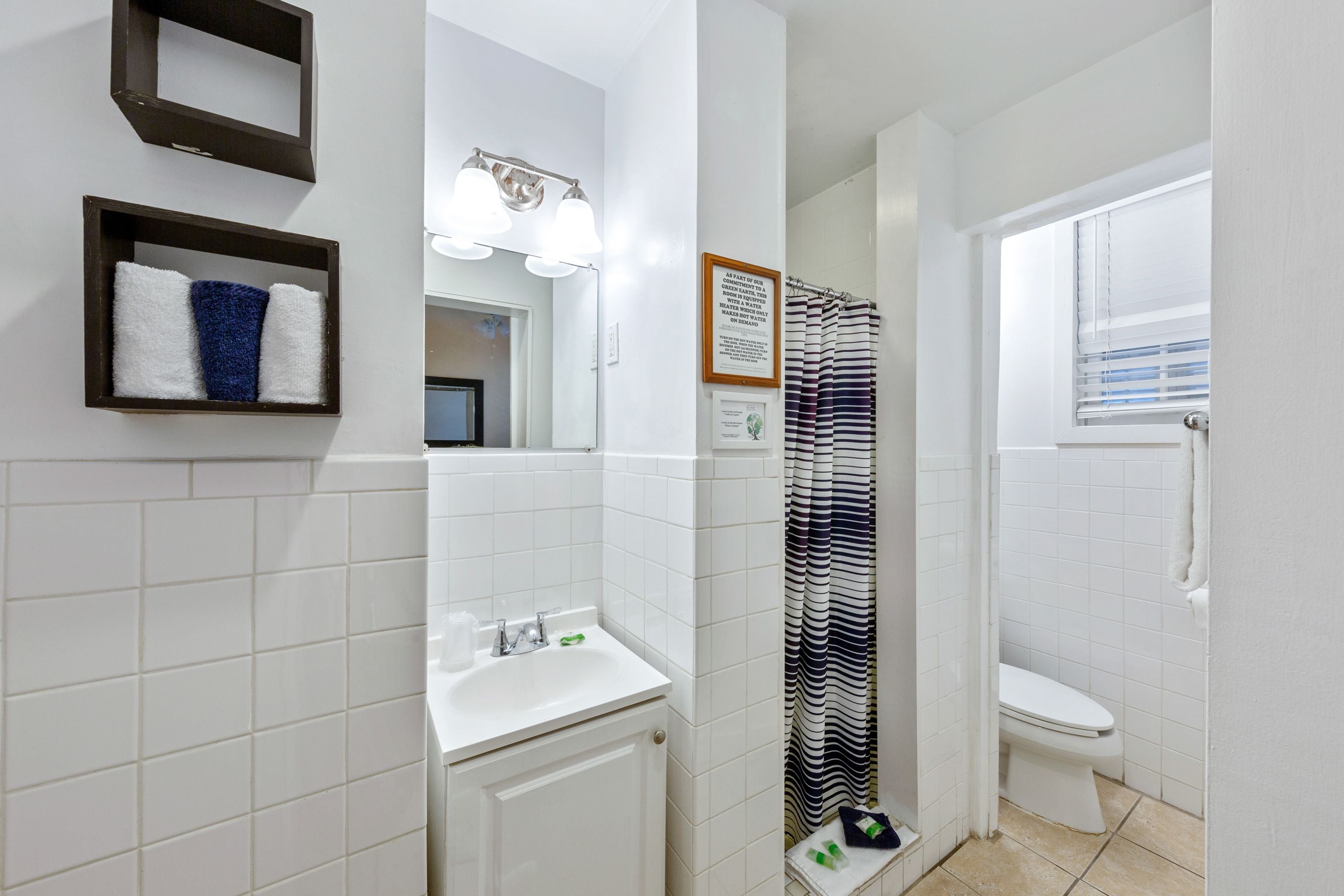 A bathroom with a white sink, a mirror, a framed quote on the wall, a striped shower curtain, and a white toilet.