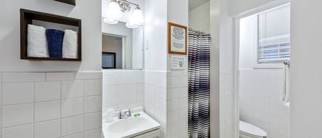 A bathroom with a white sink, a mirror, a framed quote on the wall, a striped shower curtain, and a white toilet.