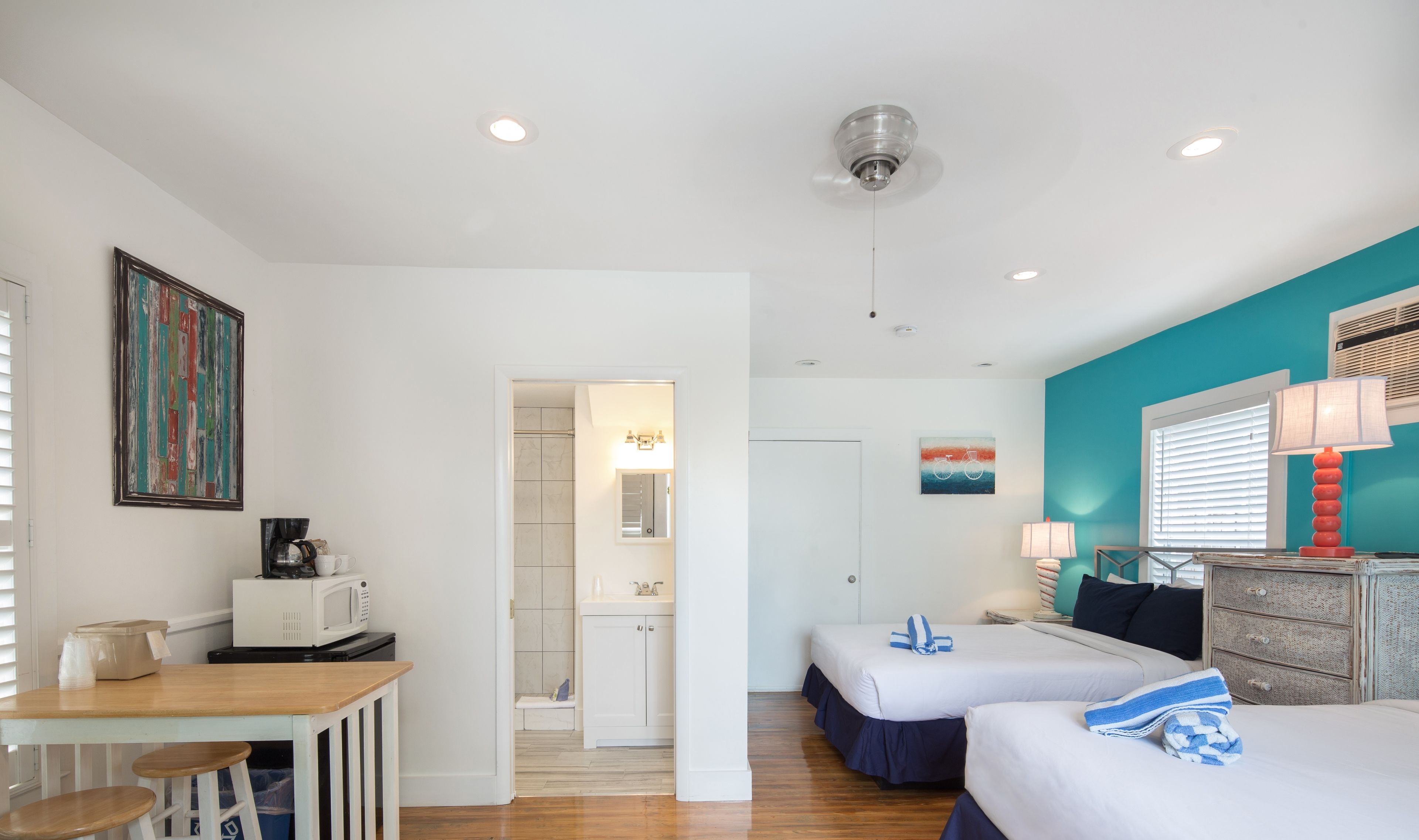 A hotel room with two beds, a desk with a microwave, a coffee maker, and a painting on the wall.