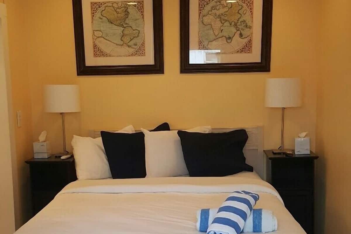 A hotel room with a bed, two nightstands, a ceiling fan, and two framed maps on the wall.