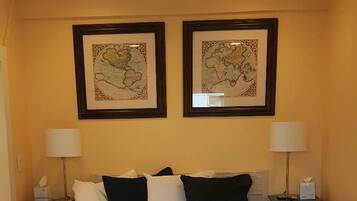 A hotel room with a bed, two nightstands, a ceiling fan, and two framed maps on the wall.